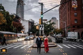 In Dumbo at dusk, the couple strolls through the city streets dressed in striking red and navy outfits, their coordinated attire and purposeful steps reflecting their unity and the energetic, urban backdrop surrounding them.